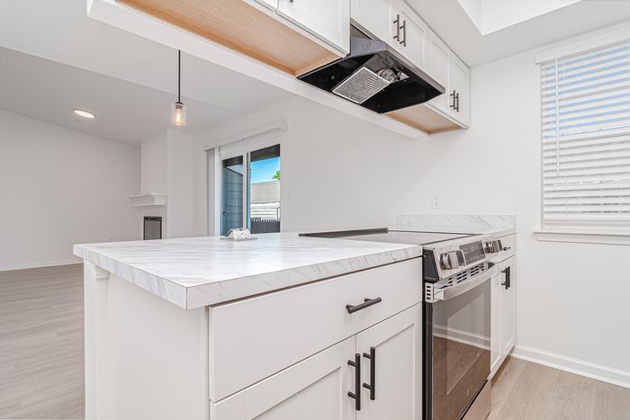 Elegant modern kitchen with sleek white cabinetry, marble countertops, and stainless steel appliances, flooded with natural light from large windows.