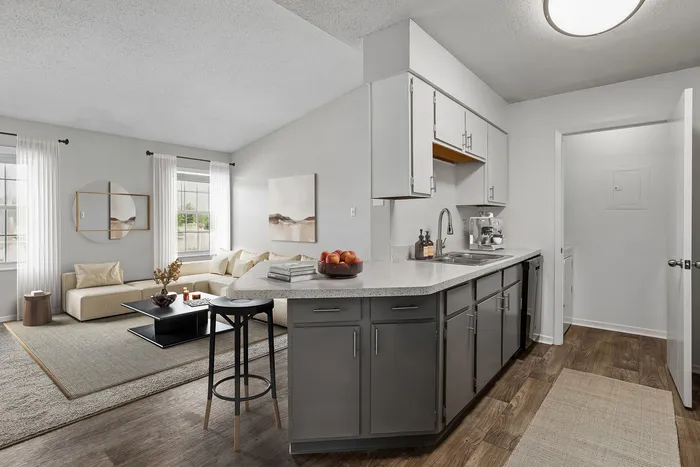 Modern open-plan living space with sleek kitchen island, stylish gray cabinets, and cozy lounge area featuring natural light and art decor.