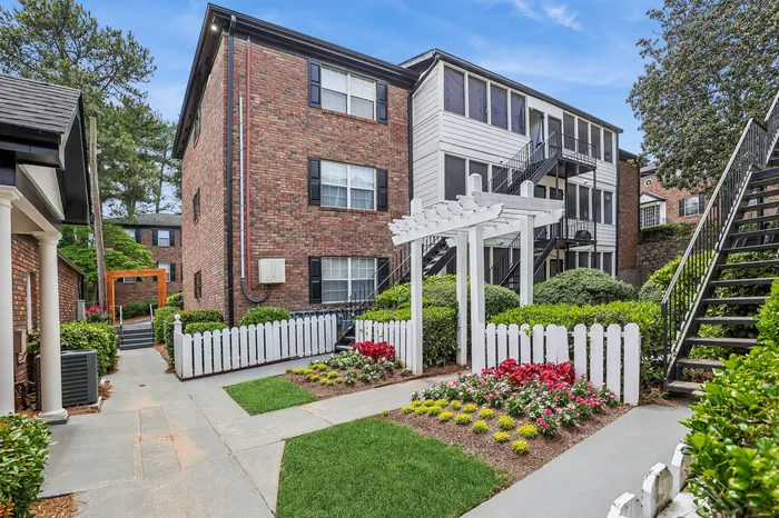 Charming brick apartment building with lush landscaping and white picket fences, offering a serene living environment with convenient stair access.