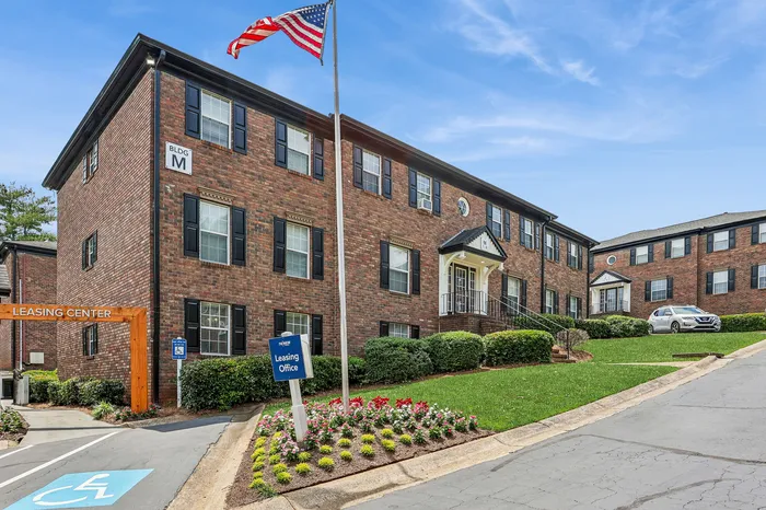 Charming brick apartment building with lush landscaping and a welcoming leasing center under a clear blue sky.