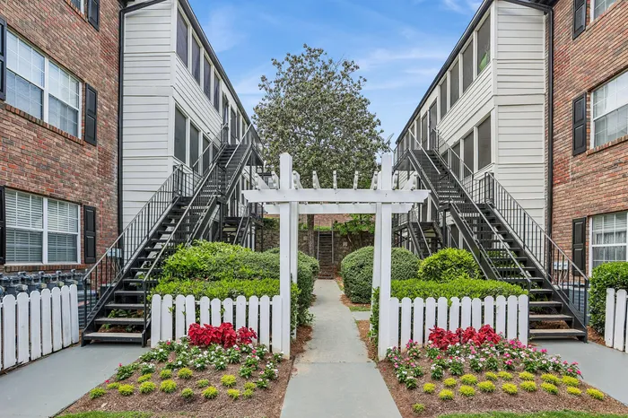 Charming apartment exterior with classic red brick facade and lush landscaping, featuring a welcoming pathway under a white pergola.
