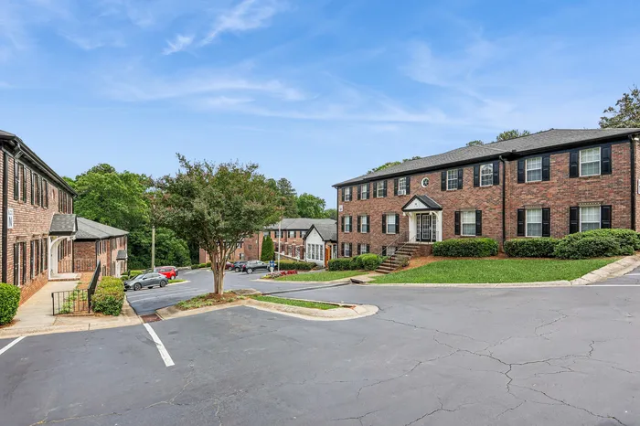Charming brick apartment complex with lush landscaping and ample parking, nestled in a serene and inviting environment.