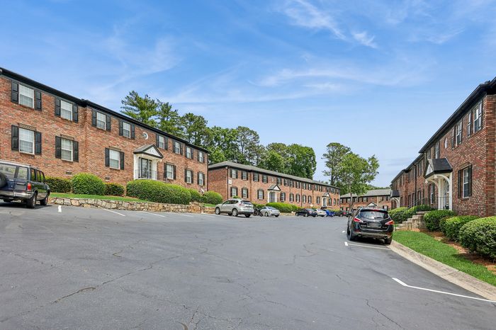 Charming brick apartment complex with well-maintained landscaping and spacious parking, basking under a clear blue sky.
