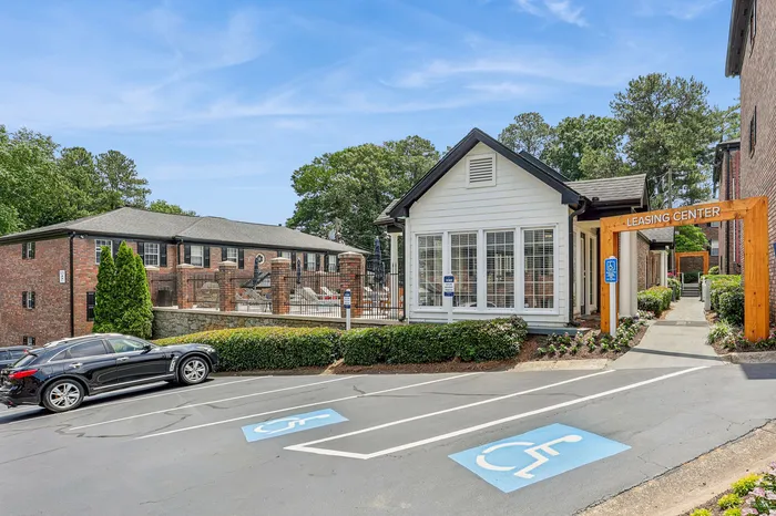 Charming leasing center with modern design, surrounded by lush greenery and convenient parking, showcasing inviting apartment complex.