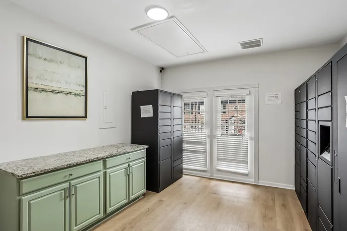 Bright and modern package room with green cabinetry and sleek black lockers, featuring large windows and elegant artwork, perfect for organized living.