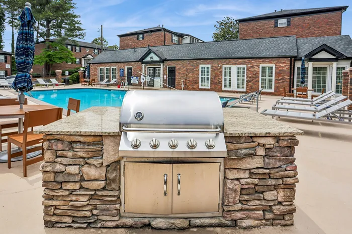Inviting poolside atmosphere featuring a stylish outdoor grill and comfortable lounge chairs, with charming brick buildings in the background.
