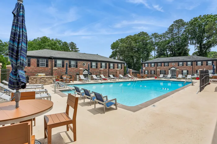 Charming apartment complex featuring a sparkling swimming pool surrounded by sun loungers and lush greenery.