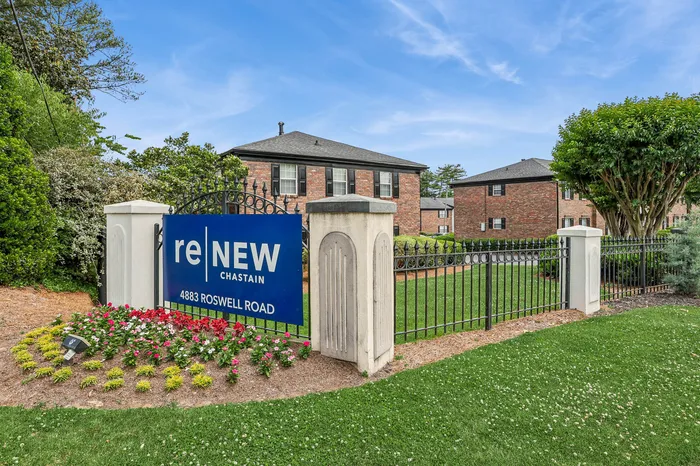 Inviting exterior of reNew Chastain apartments with lush greenery, vibrant flowers, and elegant brick architecture.