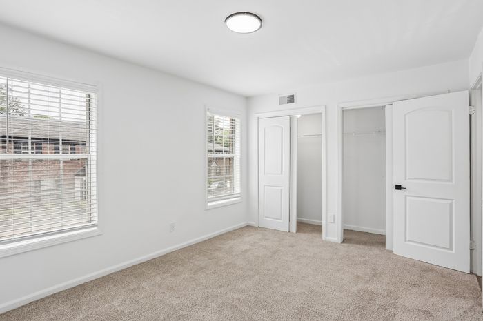 Bright and airy bedroom with soft carpet flooring, dual closets, and large windows offering natural light.