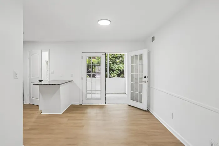 Bright and welcoming living area with elegant wood flooring, opening to a serene outdoor space through sleek glass French doors.