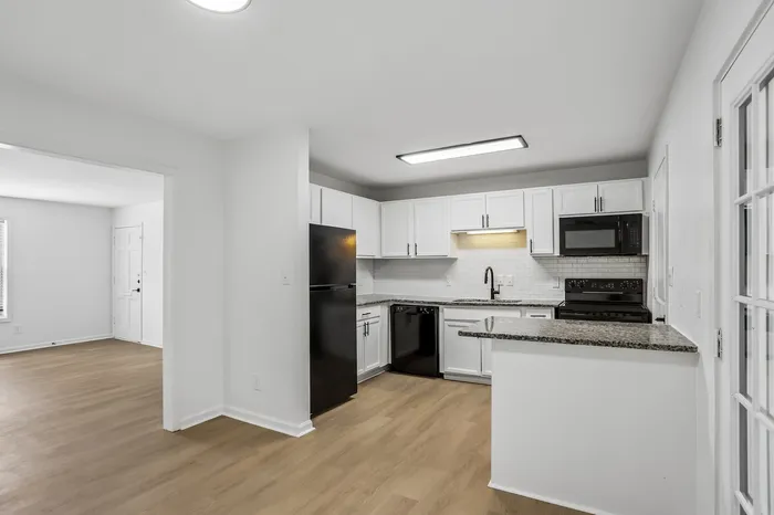 Modern kitchen with sleek white cabinetry, granite countertops, and stainless steel appliances, seamlessly opening into a bright living space with hardwood floors.