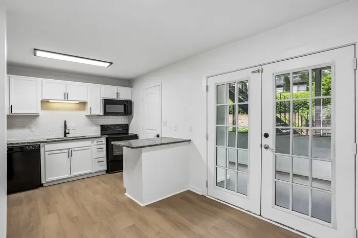 Modern kitchen with sleek white cabinetry, granite countertops, and bright double French doors leading to an outdoor space.