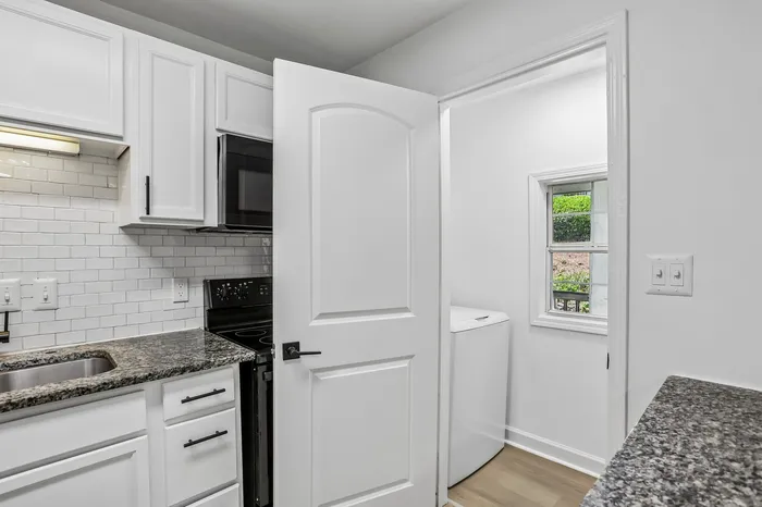 Charming kitchen with sleek granite countertops, modern appliances, and stylish white cabinetry leading into a bright laundry room with a small window view.