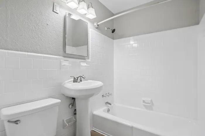 Bright, modern bathroom featuring sleek white tiles, elegant pedestal sink, and inviting bathtub.