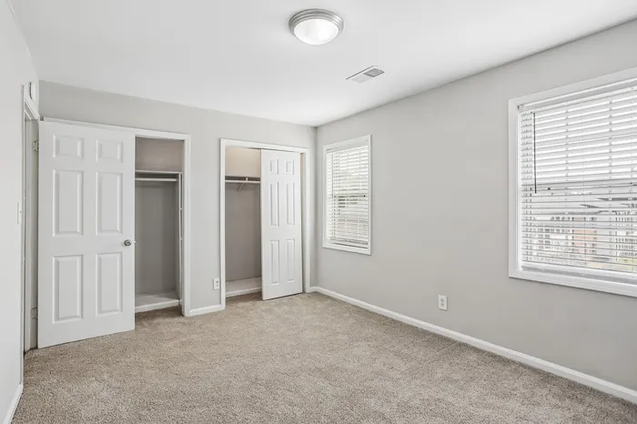 Bright and airy bedroom with plush carpeting, featuring dual closets and large windows for natural light.