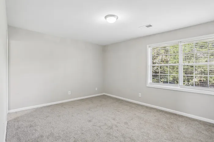 Bright and spacious bedroom with plush carpet and large windows, offering a serene ambiance and lush greenery views.