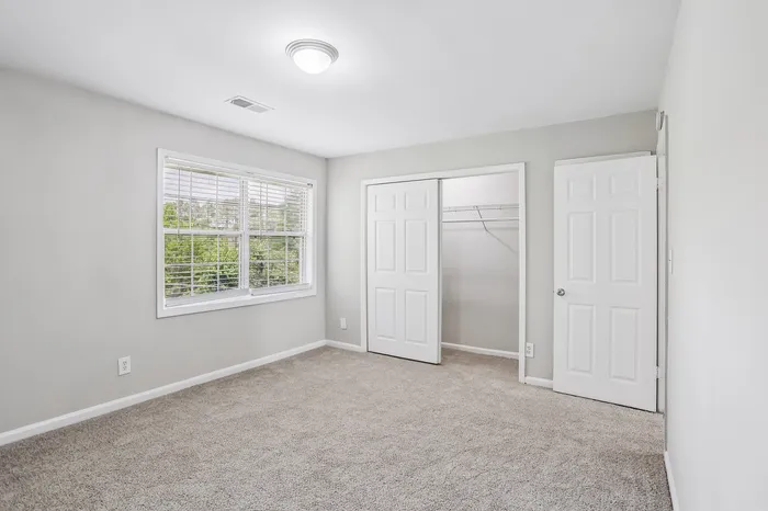 Bright and airy bedroom featuring plush carpet, fresh neutral paint, and ample closet space with double doors.