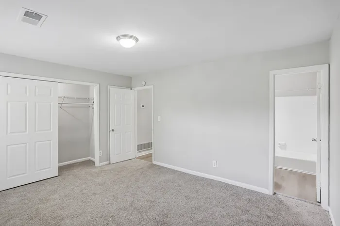 Bright and inviting bedroom with plush carpeting, spacious closet, and access to a modern bathroom.