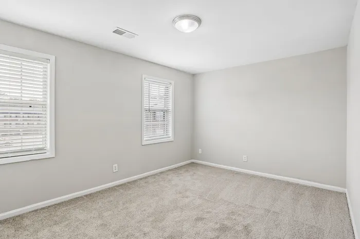 Bright and airy bedroom with soft carpet flooring and large windows for natural light.