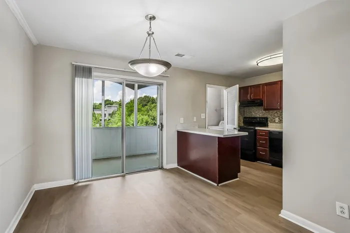 Modern apartment interior featuring an open kitchen with cherry cabinets and a cozy dining area adjacent to a bright balcony view.