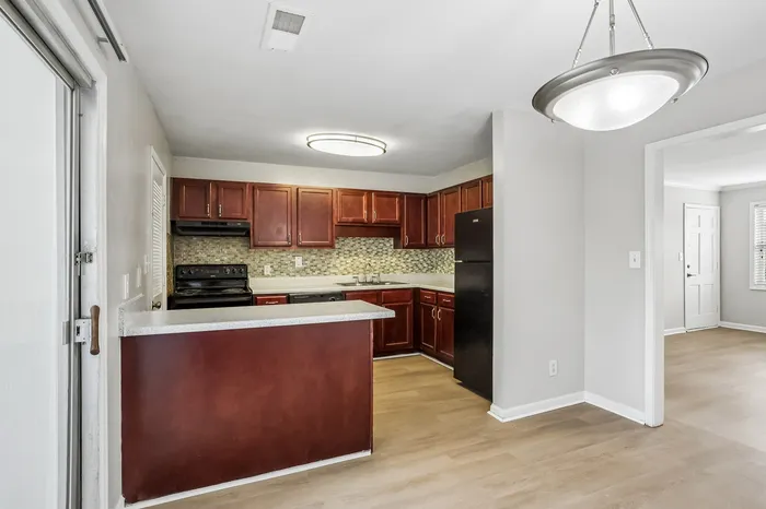 Modern apartment kitchen with rich wooden cabinetry, sleek black appliances, and stylish tile backsplash.