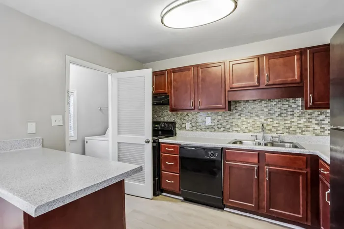 Modern kitchen with rich wooden cabinets, sleek countertops, and mosaic tile backsplash, featuring stainless steel sink and sleek appliances.