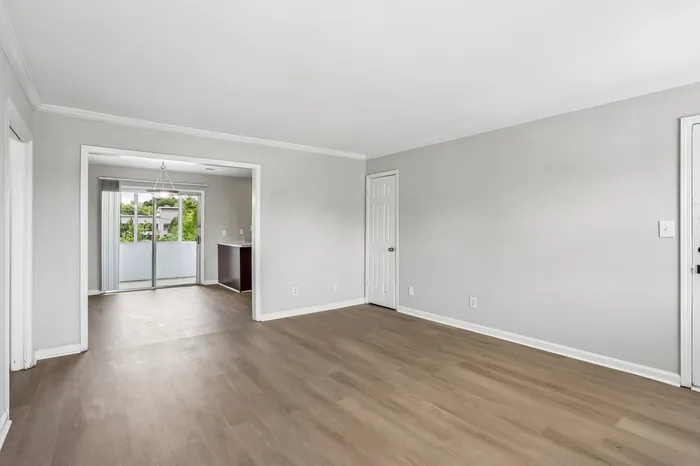 Bright and spacious living area with elegant wooden flooring, leading to a cozy balcony with lush green views.
