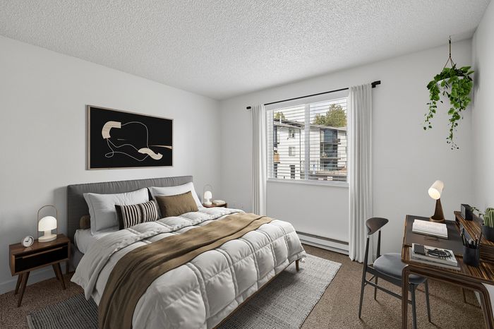 Cozy bedroom with stylish decor, highlighting a comfortable bed, modern side tables, and a desk area, illuminated by natural light through a large window.
