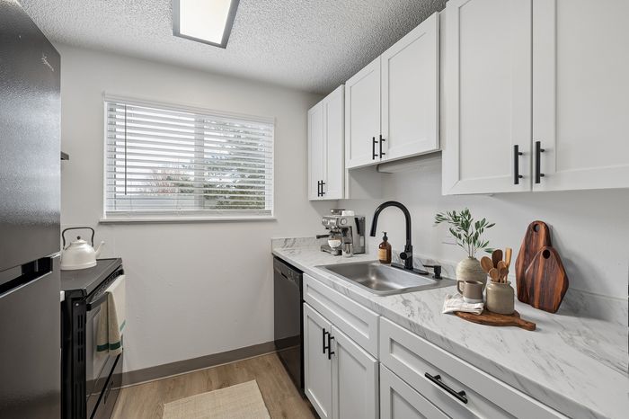 Bright modern kitchen featuring sleek white cabinetry, elegant marble countertops, and stainless steel appliances complemented by a large window for natural light.