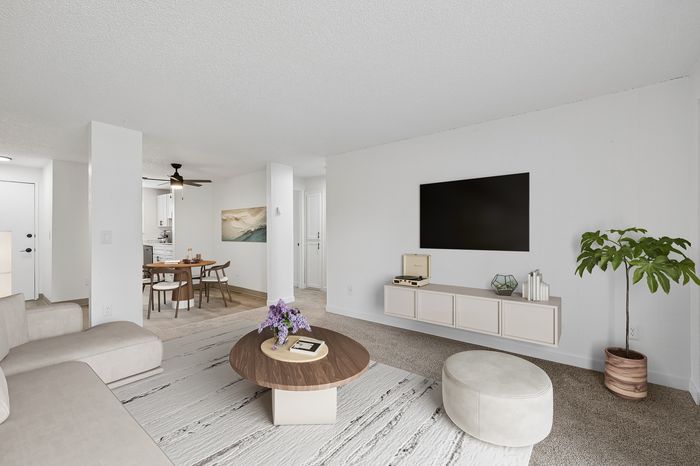 Modern living room with elegant decor including a cozy sofa, stylish coffee table, mounted TV, and dining area in the background.