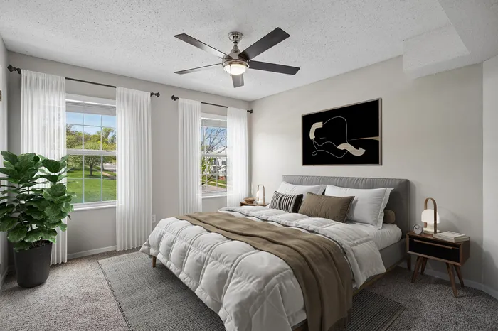Modern bedroom with large windows, elegant decor, and cozy bedding, featuring a ceiling fan and natural light.