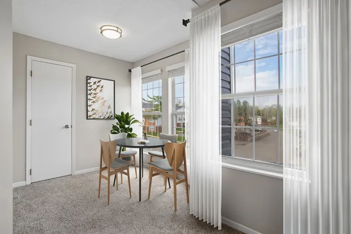 Bright dining area with large windows, sheer white curtains, and cozy seating, inviting natural light and outdoor views.