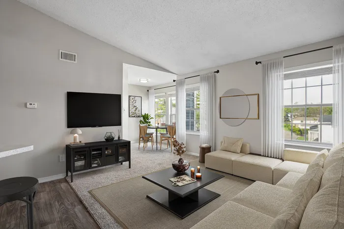 Modern living area with elegant beige sectional sofa, sleek black coffee table, and large windows offering natural light, adjacent to a cozy dining nook.