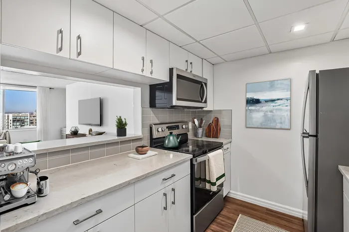 Modern kitchen with sleek cabinetry, stainless steel appliances, and elegant countertops, opening to a bright living area with city views.