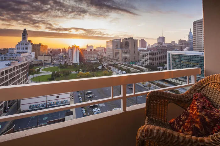 Breathtaking cityscape view from a cozy balcony at sunset, featuring vibrant urban architecture and lush greenery.