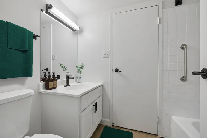 Sleek modern bathroom with elegant white fixtures, stylish black accents, and vibrant green towels for a refreshing touch.