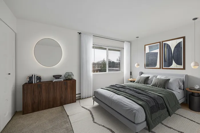 Elegant bedroom with a modern design featuring a plush bed, stylish dresser, round mirror, and ambient natural light streaming through large windows.