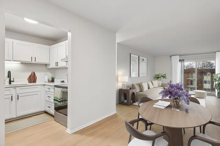 Elegant open-concept apartment featuring a stylish modern kitchen with white cabinetry and cozy living area with large windows offering abundant natural light.