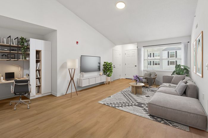Modern living room with cozy gray sectional, natural light from large window, and stylish workspace corner with shelving.