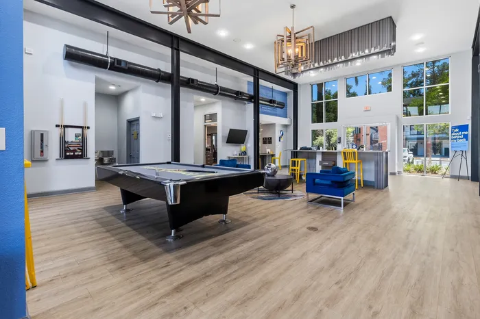 Bright and modern game room with a sleek pool table, vibrant blue chairs, and a stylish bar area featuring yellow stools.