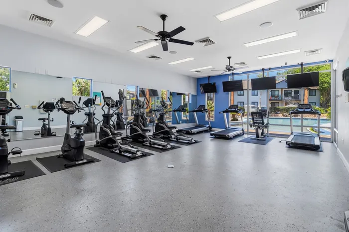 Modern fitness center with cardio equipment and large windows overlooking a sparkling swimming pool.