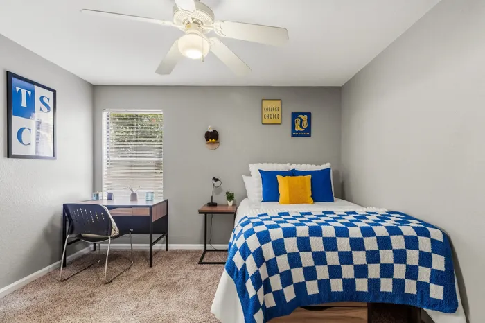 Bright and cozy bedroom featuring a plush bed with blue and white accents, a compact study desk, and vibrant wall decor.