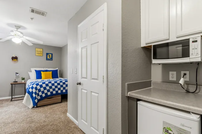 Inviting bedroom with vibrant blue and yellow accents, complete with a cozy bed and convenient kitchenette featuring a microwave.