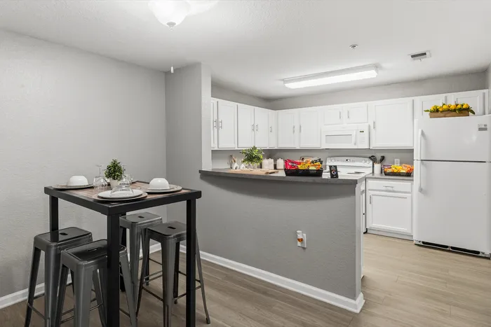 Modern kitchen with sleek white cabinets, elegant countertops, and a cozy dining area with stylish seating in an inviting apartment setting.