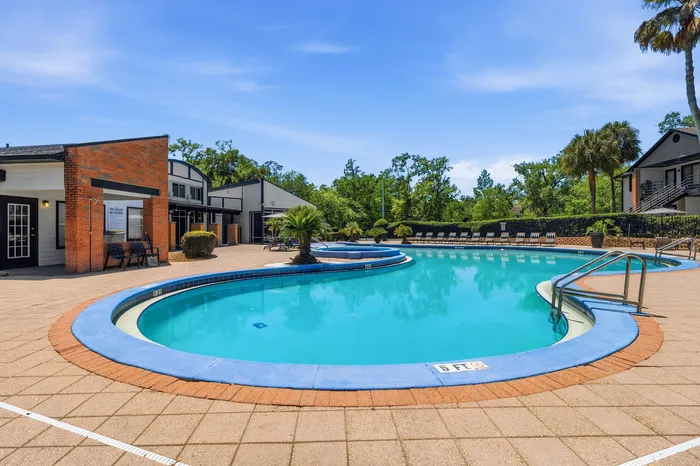 Inviting outdoor pool area with vibrant blue water, surrounded by lush greenery and modern buildings under a clear blue sky.