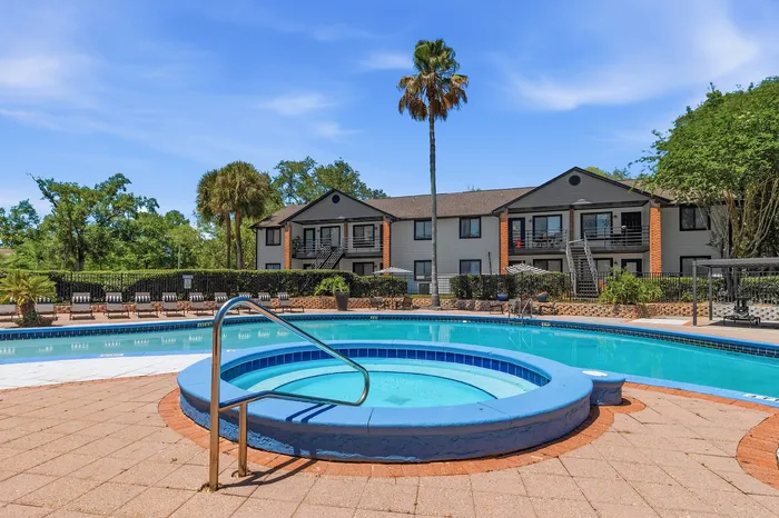 Inviting apartment complex with a sparkling pool and relaxing hot tub, surrounded by lush greenery and modern accommodations.