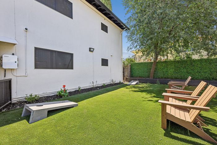 Charming outdoor space with lush green lawn, comfortable wooden chairs, and vibrant plants, perfect for relaxation and entertainment.