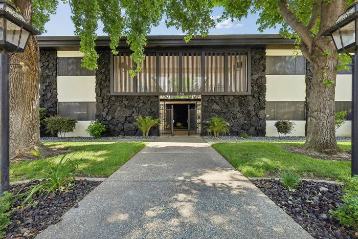 Charming building entrance with modern architectural design, surrounded by lush greenery and inviting pathways.