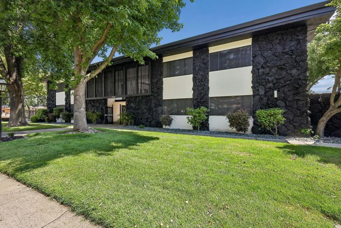 Charming apartment building with modern architecture, featuring lush green lawns and mature trees, perfect for tranquil living.