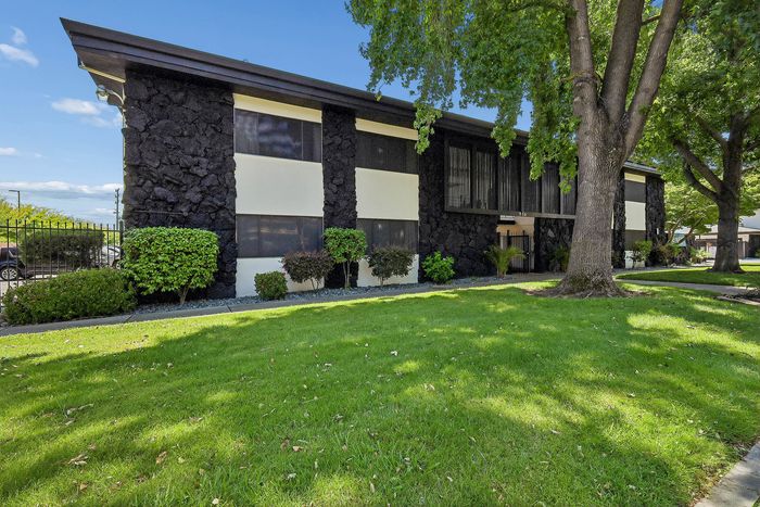 Charming apartment building with unique stone exterior, lush green lawn, and mature trees in a peaceful neighborhood setting.
